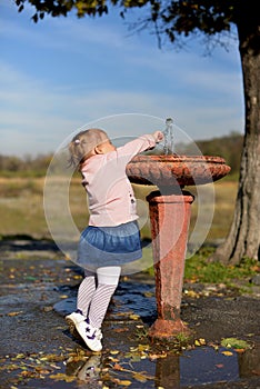 The little girl stretches to the fountain to drink water.