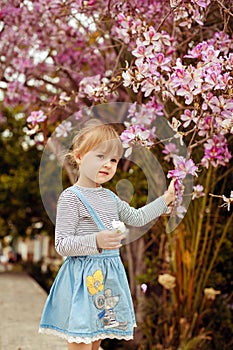 Little girl in a striped denim dress standing near a blossoming