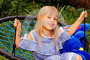 Little girl in a striped dress on a spider web swing. Lollipop in mouth.