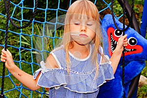 Little girl in a striped dress on a spider web swing. Lollipop in mouth.