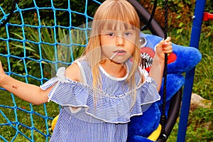 Little girl in a striped dress on a spider web swing. Lollipop in mouth.