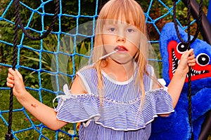Little girl in a striped dress on a spider web swing. Lollipop in mouth.