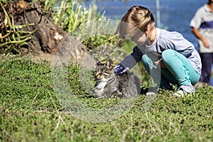 Little girl stroking a cat on the river bank