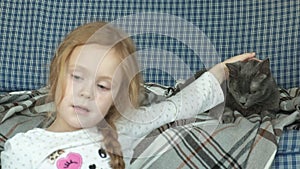 Little girl stroking a gray cat on the couch