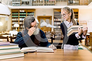 A little girl student pupil holding a lot of books in her hands and looking at her senior bearded teacher sitting at the