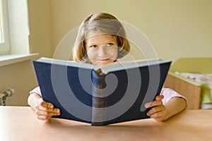 Little girl student sits at a desk with book. School, education, knowledge and children