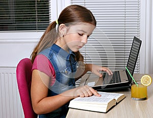 Little girl studies with a book and a laptop