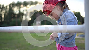 Little girl in a stylish baseball cap trying to button up her jute jaket at sunset