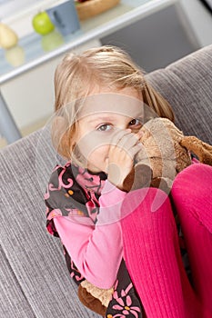 Little girl sucking thumb hugging toy dog