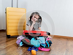 Little girl with suitcase ready for travel. Things spilled on the floor from the open suitcase.