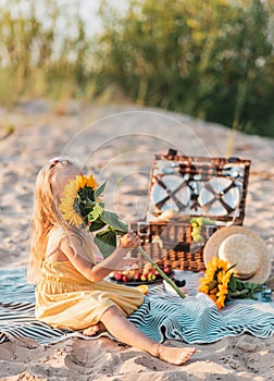 Little Girl with Sunflower, Summer picnic in the beach. Wooden basket with food