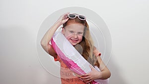 A little girl in sunglasses with a life ring invitingly winks at the camera