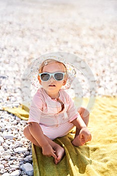 Little girl in sunglasses and panama sits on the beach