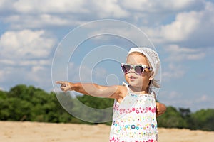 Little girl in sunglasses pointing finger hand aside and looking aside