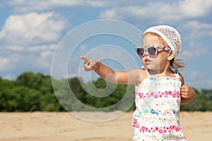 Little girl in sunglasses pointing finger hand aside and looking aside