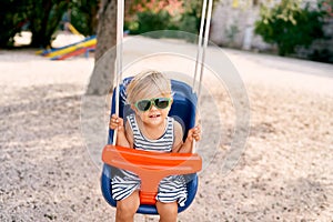 Little girl in sunglasses sits on a colorful swing