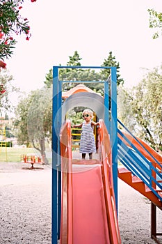 Little girl in sunglasses stands on a children slide