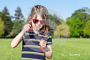 Little girl in sunglasses in summer inflates soap bubbles