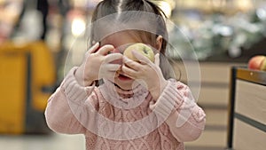 Little girl in the supermarket jokingly covers her eyes with apples.