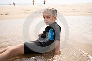 Little girl surfer in wetsuit lies ocean beach