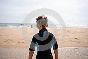 Little girl surfer in wetsuit standing ocean beach