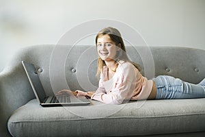 Little girl surfs on the internet lay on the sofa