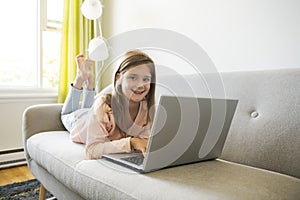 Little girl surfs on the internet lay on the sofa