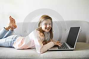 Little girl surfs on the internet lay on the sofa