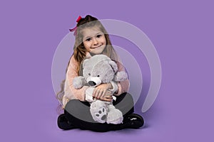 A little girl surprised as she sits with a teddy bear in her hand and holds it close to her chest because the toy is her