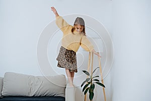 Little girl in sweater walking on a armrest of a couch, keeping balance. At home