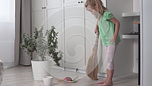 A little girl sweeps the floors of the house with a broom.