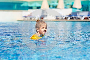 A little girl is swimming in the pool in armbands.