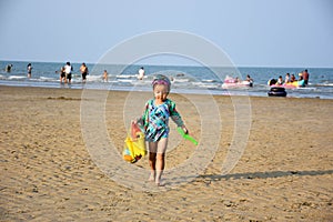 Little girl in swimming suit walk on the sand with toys