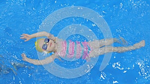 A little girl swims on her back in the pool. Child, girl learns to swim in the pool. A cute little girl is studying in