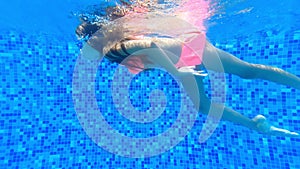 A little girl swims in an underwater pool and learns to swim. Swimming lessons for children underwater.