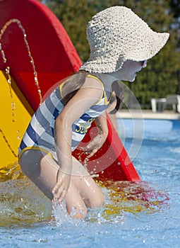 A little girl in a swimsuit and a hat sits on a water slide in the pool. Rest in warm countries. Rest at the hotel