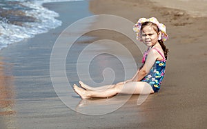 Little girl in a swimsuit is sitting on the sea beach and playing