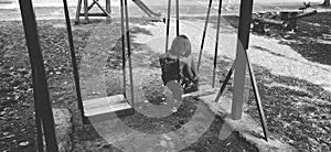 Little girl on the swing. The girl is sad alone on the playground. Monochrome black and white image. Loneliness and forgetfulness