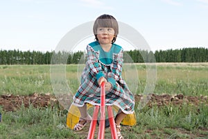 Little girl swing on seesaw at summer, funny face happy child in green dress