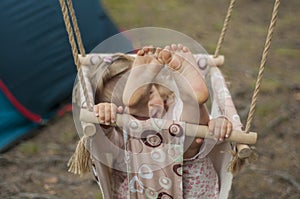 Little girl swinging on a swing. Child`s feet. Baby having fun. Camping life with a child.