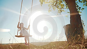 little girl swinging on a swing in the park. happy family kid dream concept. child playing in nature with a swing on