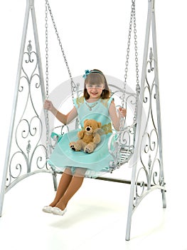 A little girl is swinging on a swing with a teddy bear.