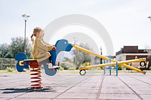 Little girl swings on a spring swing on the playground. Side view