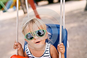 Little girl swings on a swing with her mouth open with joy