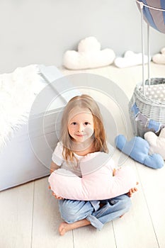 A little girl in a T-shirt and jeans holds a cloud pillow against the background of a decorative balloon. Toddler is playing in th