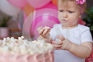 A little girl on the table with a birthday cake and balloons. The collapse of the cake. First birthday of the baby. Cakesmash