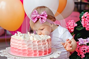 A little girl on the table with a birthday cake and balloons. The collapse of the cake. First birthday of the baby. Cakesmash