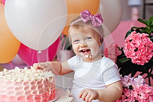 A little girl on the table with a birthday cake and balloons. The collapse of the cake. First birthday of the baby. Cakesmash