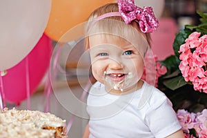 A little girl on the table with a birthday cake and balloons. The collapse of the cake. First birthday of the baby. Cakesmash