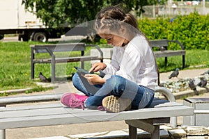 Little girl with a tablet in hands outdoors, attentively looking at the tablet screen